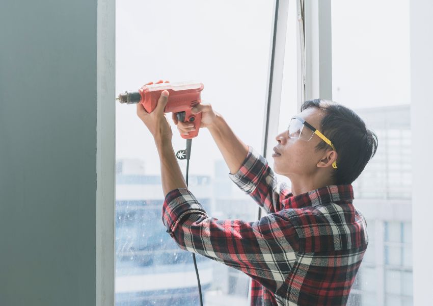 person in plaid shirt using drill to fix a window